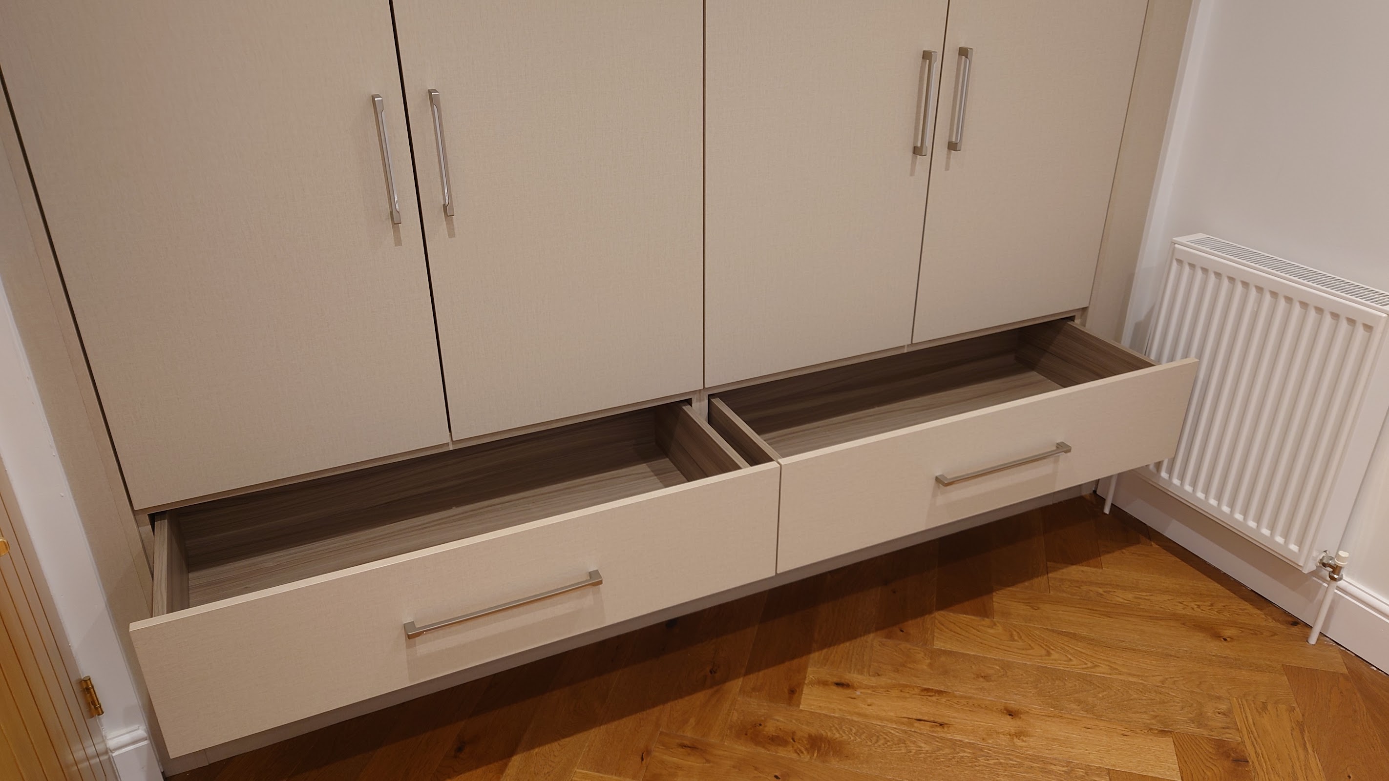 A run of made-to-measure drawers built in beneath fitted cupboards, finishing an awkward wall over herringbone flooring with useful, tucked-away storage.